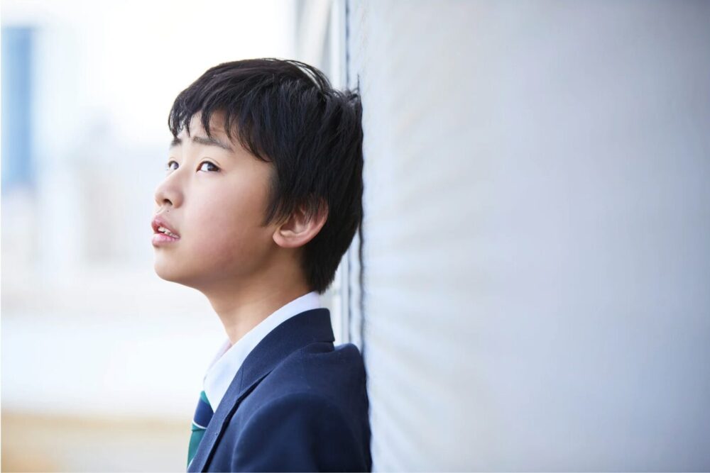 壁に寄りかかって悩んでいる中学生